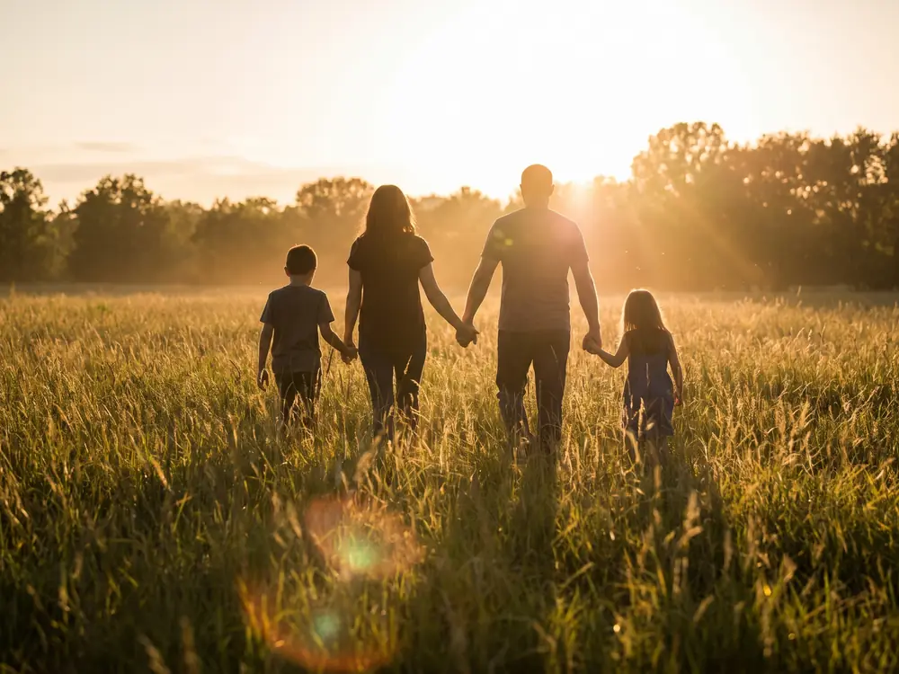 Eine Familie geht bei Sonnenuntergang über eine Wiese, von hinten gesehen