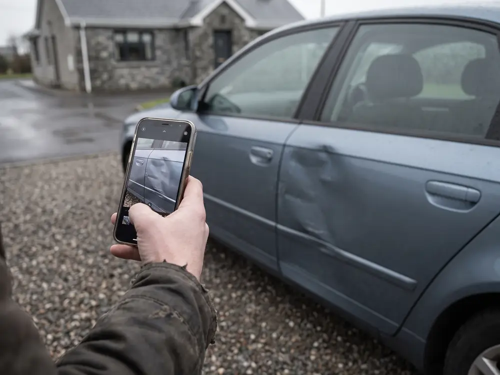 Eine Hand fotografiert mit dem Telefon eine eingedellte Autotür